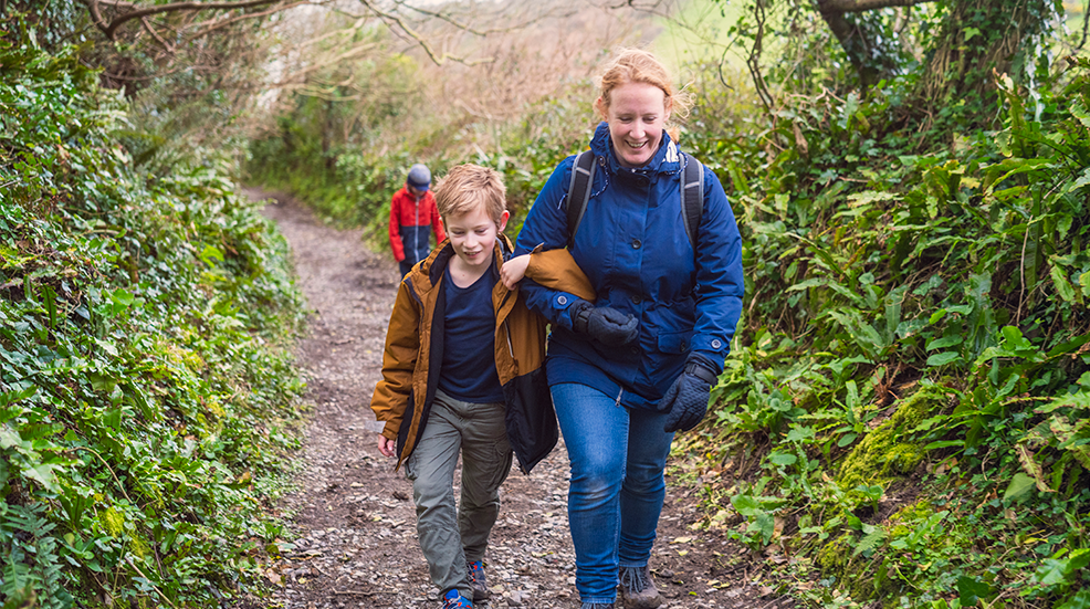 A mother and her young son smiling and chatting while walking up a steep path in the countryside in winter.
